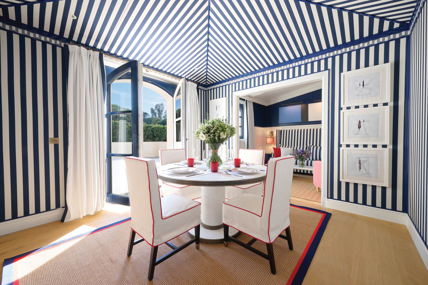 a circular table with white chairs below a striped canopy