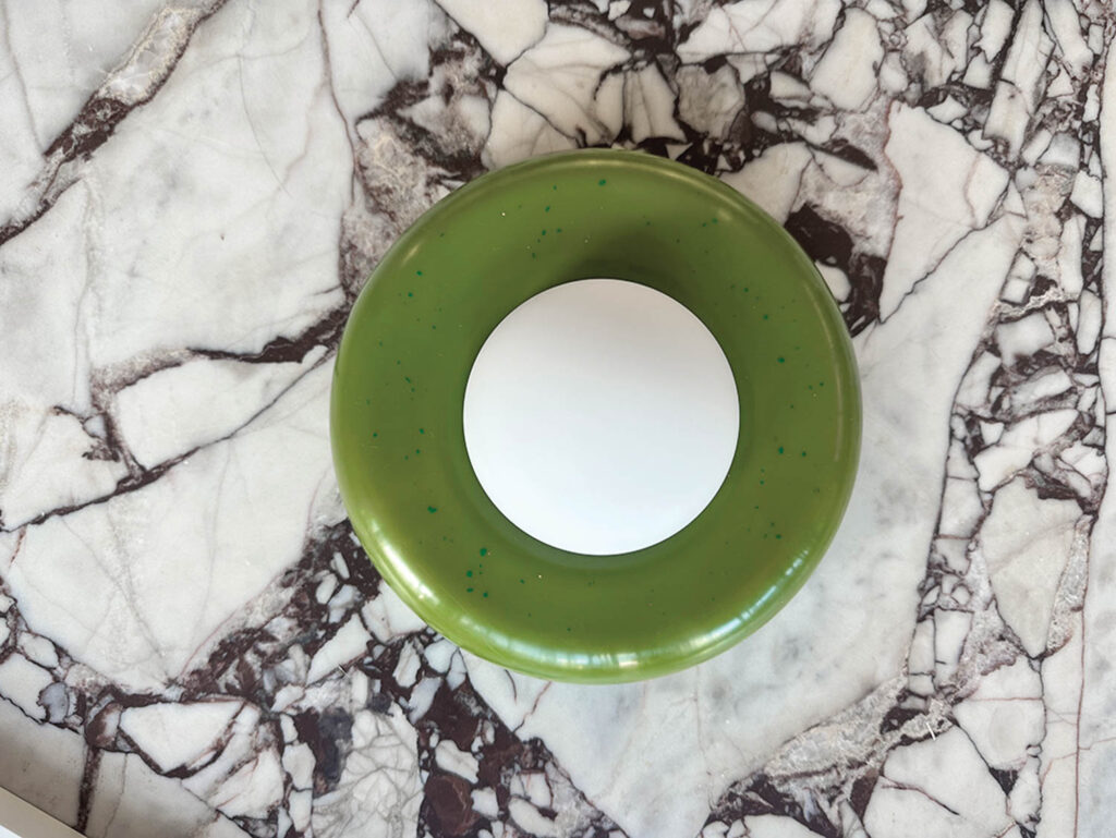 green donut-like sconce against a marble counter