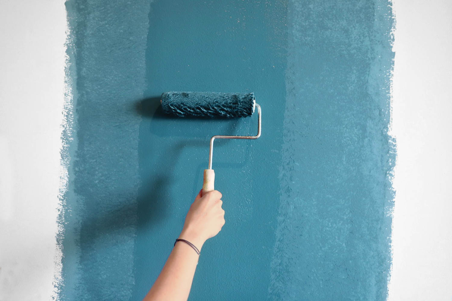person using paint roller for dark blue paint against walls