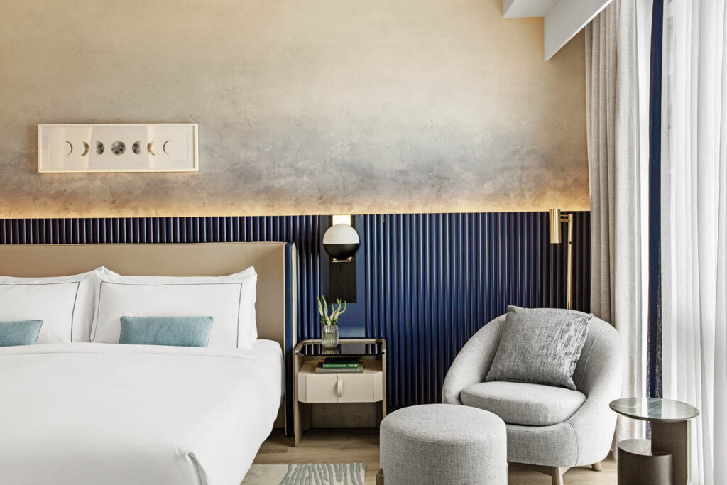 standard guest room with large white bed, cloud-like wallpaper and grey chair